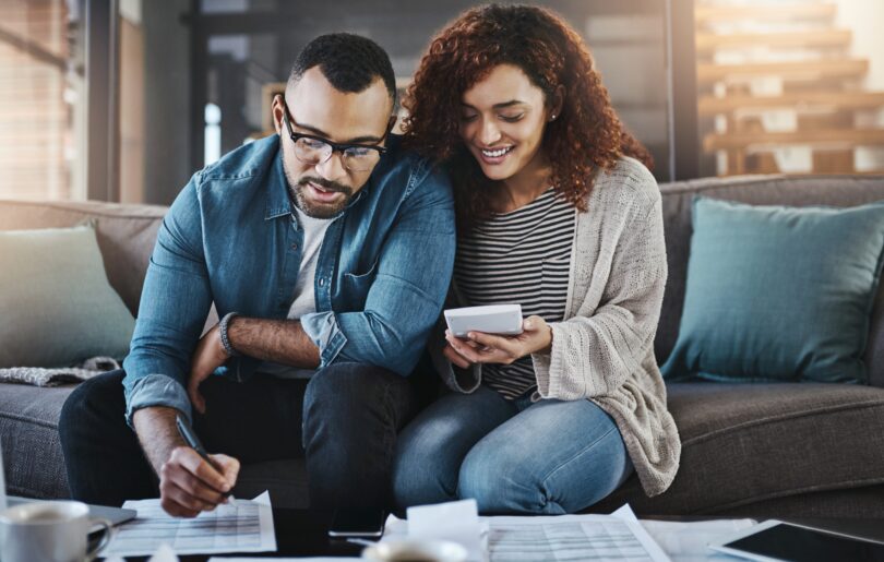 A man and a woman look at the costs of their mortgage on a sofa with paper and calculators 