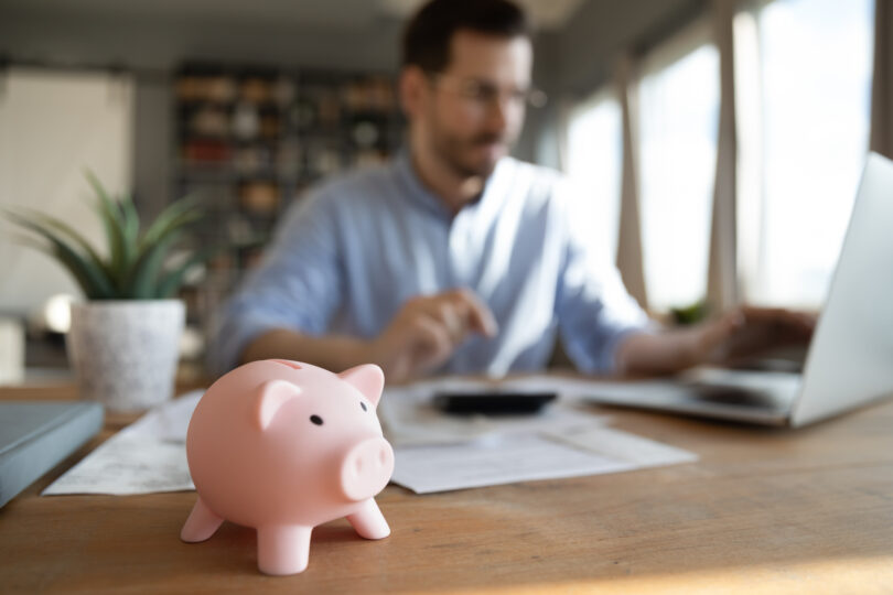 A man sits at his desk with a piggy bank on it