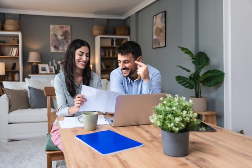 two people happily look at documents and their computer at home