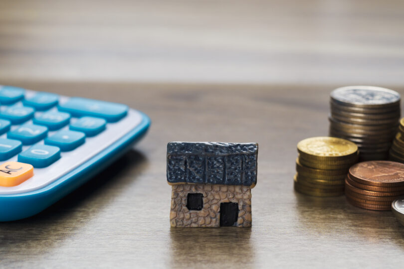 A UK landlord calculating buy-to-let mortgage options with a model house and paperwork, representing new TMW mortgage rate reductions.